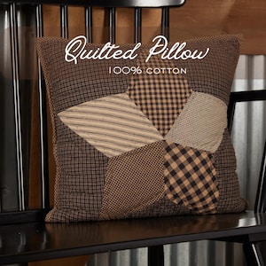 May include: A brown quilted pillow with a patchwork design featuring various patterns, including stripes and checks. The pillow is made of 100% cotton and is placed on a black chair. The text "Quilted Pillow" and "100% Cotton" are visible on the pillow.