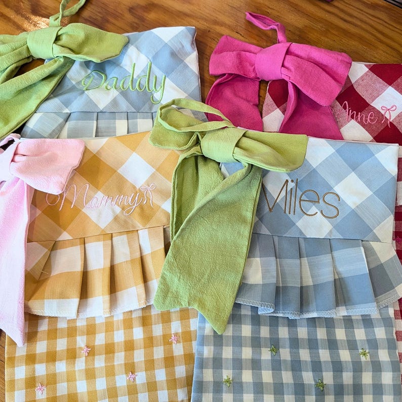 a collection of colorful aprons or chef's uniforms, each with a name embroidered on them. The aprons are arranged on a wooden surface, creating a visually appealing display.