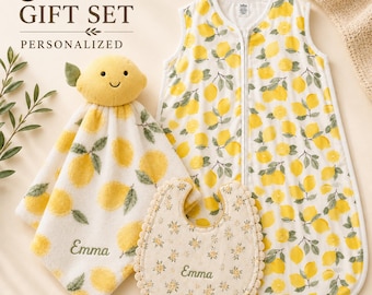 May include: A 3 piece personalised gift set featuring a sleeveless wearable blanket, a lemon-shaped security blanket, and a bib. All items feature a yellow lemon print. The security blanket and bib are embroidered with the name Emma.