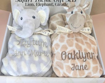May include: A gift box containing two plush animal security blankets. One is a gray elephant with the embroidered name Taytum Ann Marie, and the other is a tan giraffe with the name Oaklynn Jane. Text reads: Safari Theme Gift Sets Lion, Elephant, Giraffe.