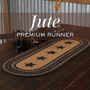 Pode incluir: Um caminho de mesa oval de juta trançada com um centro castanho natural, cinco motivos de estrelas pretas e uma borda trançada preta espessa. O texto Jute PREMIUM RUNNER está sobreposto na imagem. O caminho está sobre uma mesa de madeira.
