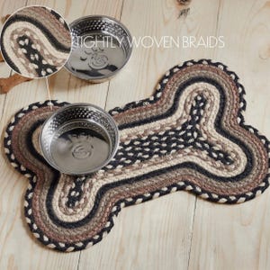 Handwoven Braided Pet Mat offers floor protection with rustic farmhouse style. Jute natural fiber placemat shaped like a dog bone complements kitchen decor and promotes sustainable living. May include: A dog bone-shaped braided rug in shades of brown, beige, and black, with two stainless steel dog bowls. The rug features tightly woven braids and is designed for pet feeding areas.