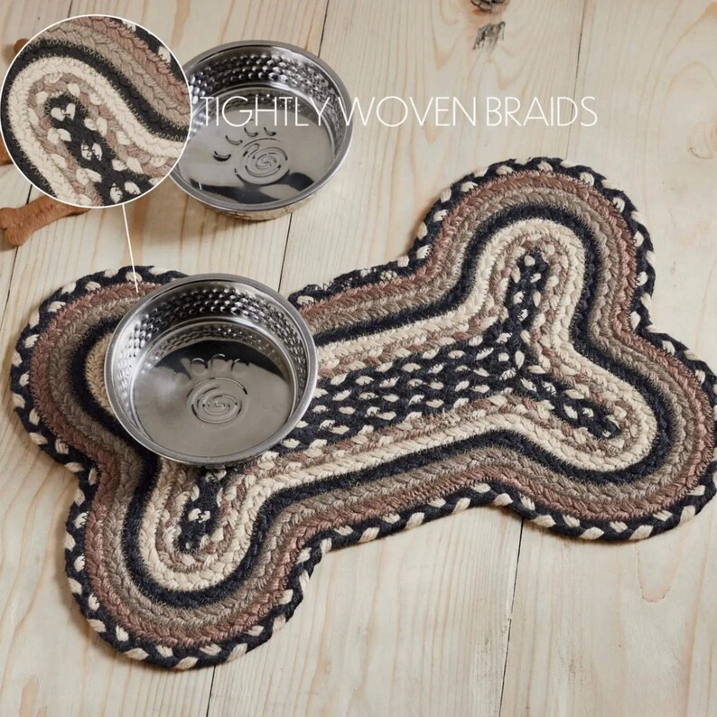 Handwoven Braided Pet Mat offers floor protection with rustic farmhouse style. Jute natural fiber placemat shaped like a dog bone complements kitchen decor and promotes sustainable living. May include: A dog bone-shaped braided rug in shades of brown, beige, and black, with two stainless steel dog bowls. The rug features tightly woven braids and is designed for pet feeding areas.