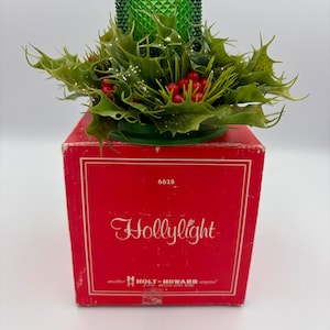 May include: A vintage "Hollylight" candle holder with a green glass top and a holly and berry arrangement. The candle holder sits on a red box with the text "Hollylight" in script. The box is marked "another HOLT-HOWARD original".