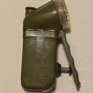 May include: An olive green vintage Daco-Lite flashlight with a clear, ridged lens. The flashlight has a metal clip and the text "Daco-Lite" and "Dayton Acme Co. Cincinnati, Ohio, U.S.A." is visible on the body.