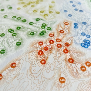 Puede incluir: Un mapa topogr&aacute;fico detallado con l&iacute;neas de contorno en tonos de naranja, verde, azul y amarillo. Numerosos c&iacute;rculos numerados est&aacute;n dispersos por el mapa, indicando ubicaciones espec&iacute;ficas. El mapa est&aacute; impreso sobre una superficie blanca.
