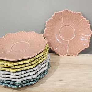 May include: A stack of six floral-patterned ceramic saucers in shades of pink, green, blue, and gray. The saucers are stacked with the pink one on top and the blue one on the bottom.