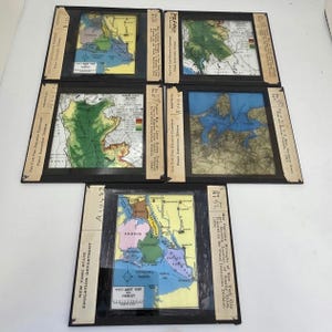 May include: A collection of vintage map slides from the New York State Education Department. The slides feature colorful geographical outlines of various regions, including New York City boroughs. Each slide is encased in a black frame with attached labels.