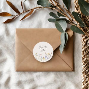 May include: A kraft paper envelope with a round sticker featuring floral illustrations and the text "Custom Text Here." The sticker has a cream background with colorful wildflowers. Eucalyptus and decorative elements are in the background.