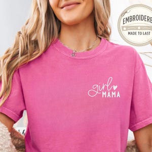 Puede incluir: Una camiseta rosa fucsia de manga corta con las palabras "girl mama" en escritura blanca. La camiseta tiene cuello redondo y un corte holgado. El texto "EMBROIDERED MADE TO LAST" est&aacute; en un dise&ntilde;o circular en la parte superior derecha.