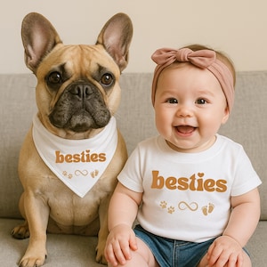 May include: A French Bulldog wearing a white bandana with the word "besties" in orange. A baby wearing a white t-shirt with the word "besties" in orange, paw prints, an infinity symbol, and footprints. The baby is wearing a pink bow.