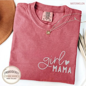 Puede incluir: Una camiseta de color sand&iacute;a con las palabras bordadas "girl MAMA" y un peque&ntilde;o coraz&oacute;n. La camiseta tiene una etiqueta Comfort Colors y un collar plateado con un colgante. Una pegatina redonda con las palabras "EMBROIDERED MADE TO LAST" est&aacute; en la esquina inferior izquierda.