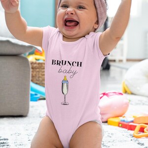 May include: A pink baby onesie with the text "BRUNCH baby" and a champagne glass with a baby bottle nipple.