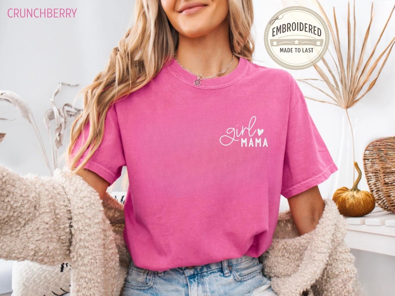 Puede incluir: Una camiseta rosa fucsia de manga corta con las palabras "girl mama" en escritura blanca. La camiseta tiene cuello redondo y un corte holgado. El texto "EMBROIDERED MADE TO LAST" est&aacute; en un dise&ntilde;o circular en la parte superior derecha.
