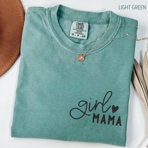 Puede incluir: Una camiseta Comfort Colors verde claro con las palabras "girl mama" en escritura negra. Un collar dorado con un peque&ntilde;o colgante est&aacute; drapeado sobre la camiseta. La camiseta es talla small.