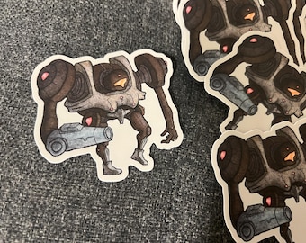 May include: A sticker featuring a cartoon robot with a gun. The robot is gray and black with a white chest plate. The robot is holding a gun in its right hand. The sticker is on a gray fabric background.