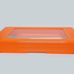 以下が含まれることがあります： 透明な窓が付いたオレンジ色のプラスチックケース。ケースは小型の電子機器を入れるように設計されています。