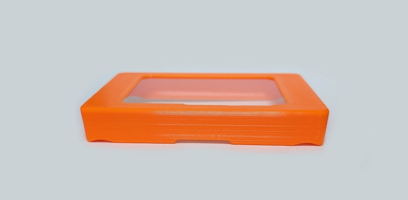 以下が含まれることがあります： 透明な窓が付いたオレンジ色のプラスチックケース。ケースは小型の電子機器を入れるように設計されています。