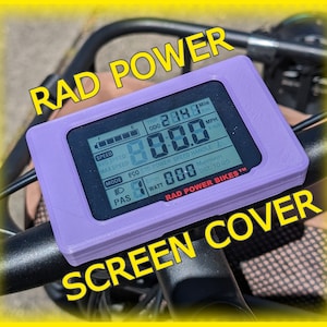 以下が含まれることがあります： Rad Power Bikes 電動自転車のディスプレイ用の紫色のプラスチック製スクリーンカバー。ディスプレイには速度、走行距離、その他の情報が表示されます。スクリーンカバーのテキストには「RAD POWER BIKES&trade;」と表示されています。