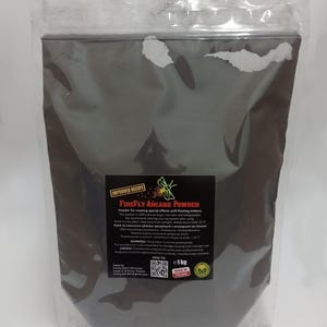 Peut inclure: Un sac en plastique transparent contenant de la poudre Firefly Arcane, une poudre gris foncé pour créer des effets spéciaux. Le sac porte une étiquette avec du texte et un logo vert. Le sac contient 1 kg de poudre.