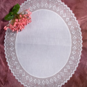 May include: White crocheted doily with a delicate floral pattern. A cluster of pink flowers is placed on the doily.