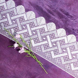 Puede incluir: Borde de encaje blanco tejido a crochet con un patrón geométrico, sobre un fondo de tela púrpura con una rama de flores rosas.