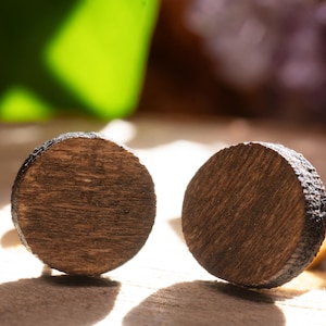 Puede incluir: Un par de pendientes redondos de madera con un acabado de madera de grano marrón oscuro.