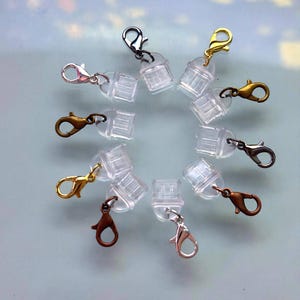 Peut inclure: Un ensemble de fermoirs mousquetons en plastique transparent avec différentes finitions métalliques, or, argent et bronze. Ces petits fermoirs sont destinés à la fabrication de bijoux et aux projets d'artisanat.