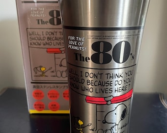 May include: Stainless steel tumbler featuring Snoopy from the Peanuts comic strip. The tumbler has the text "The 80's" and "Well, I don't think you should because do you know who lives here?" along with other text and graphics.
