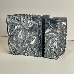 May include: Two bars of black and white marbled soap. The soap is stacked on top of each other. The soap has a swirl pattern.