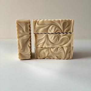 May include: Four bars of handmade soap stacked on top of each other. The soap is a light brown color with a swirl pattern.