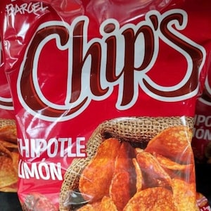 May include: A red bag of chips with the word "Chips" in large white and brown letters. The bag features a burlap sack graphic filled with chips. The flavor is "Chipotle Limon".