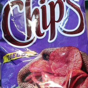 May include: A purple bag of chips with the word "Chips" in large, white and maroon letters. The bag contains red chips in a woven basket. The word "WEL" is visible on the bag.