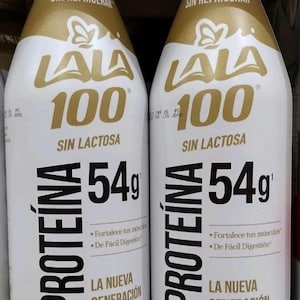 May include: Two white plastic bottles of LALA 100 protein drink. The bottles have gold and black text, including "PROTEÍNA" and "54g". The label also states "SIN LACTOSA" and "LA NUEVA GENERACIÓN DE LECHES".