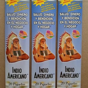 May include: Three identical vertical rectangular packages of incense sticks. Each blue package features a yellow starburst with text, an illustration of a person in a feathered headdress, and the text Indio Americano, 20 Pajuelas, and Exito.