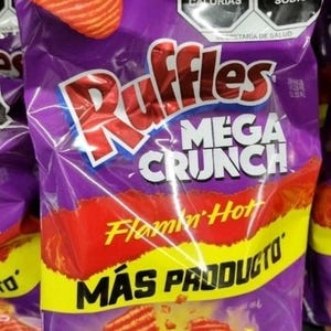 May include: A purple bag of Ruffles Mega Crunch potato chips with a Flamin' Hot flavor. The bag features a large red "Ruffles" logo and the words "MEGA CRUNCH" in white. The bag also has a yellow stripe with the words "MÁS PRODUCTO".