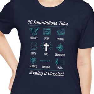 May include: Navy blue t-shirt with teal graphics and text. The shirt features illustrations and words related to subjects like history, math, and science. The text "CC Foundations Tutor" and "Keeping it Classical" are also displayed.