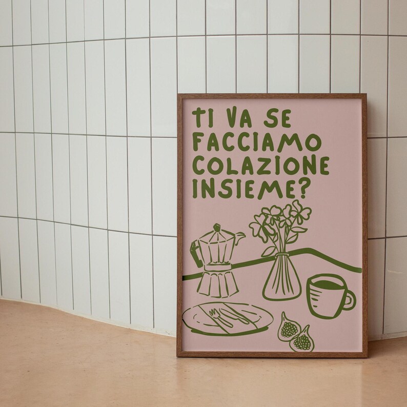 May include: A pink framed print with the text "Ti va se facciamo colazione insieme?" in green. The print features a green illustration of a coffee pot, a vase of flowers, a plate with cutlery, and a cup of coffee.