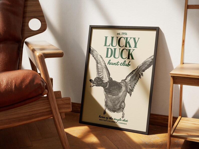 Puede incluir: L&aacute;mina enmarcada con una ilustraci&oacute;n de un pato en vuelo. El texto "LUCKY DUCK hunt club" es verde, con "est. 1956" arriba y "home of the single shot, BRITISH COLUMBIA, CANADA" abajo, sobre un fondo crema.