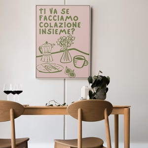 May include: A pink and green illustration of a breakfast scene with a coffee pot, a cup of coffee, a plate with cutlery, a vase of flowers, and figs. The text reads "Ti va se facciamo colazione insieme?"