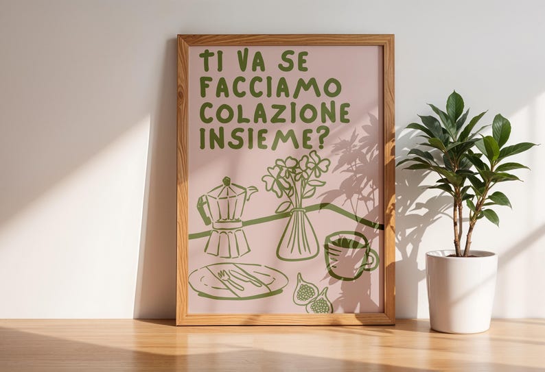 May include: A framed print with a pink background and green text that reads "Ti va se facciamo colazione insieme?"  The print features a green illustration of a coffee pot, a vase of flowers, a cup of coffee, and figs.