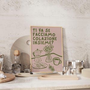 May include: A pink and green illustrated poster with the text "Ti va se facciamo colazione insieme?"  The poster features a coffee pot, a vase of flowers, and a cup of coffee.