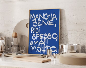 May include: A framed blue print with the Italian phrase "Mangia Bene, Ridi Spesso, Ama Molto" in white handwritten style. The print is in a gold frame and is displayed on a kitchen counter with other kitchen items.