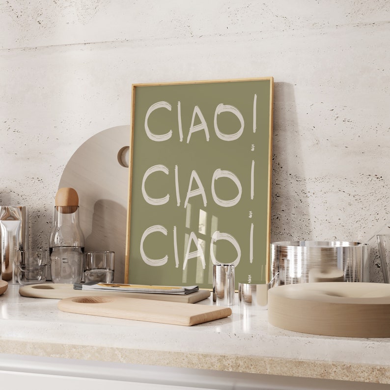 May include: A framed print with a green background and the word "CIAO" written three times in white. The print is sitting on a worktop with other decorative items.