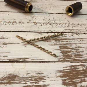 Peut inclure: Deux &eacute;tuis en bois avec des accents en laiton et deux pi&egrave;ces en m&eacute;tal torsad&eacute; dor&eacute;es sur une surface en bois blanc.