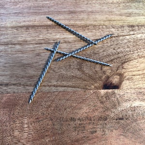 May include: Three silver twisted metal rods on a wooden surface.