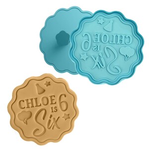 Peut inclure: Deux emportes-pièces en plastique bleu. Le plus grand est en forme de cercle avec un bord festonné et comporte le texte "CHLOE is Six" avec une étoile, un chapeau de fête et un ballon. Le plus petit est un cercle simple avec un bord festonné.