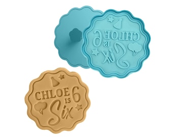 May include: A set of two blue plastic cookie cutters. The larger cutter is shaped like a circle with a scalloped edge and features the text "CHLOE is Six" with a star, a party hat, and a balloon. The smaller cutter is a plain circle with a scalloped edge.