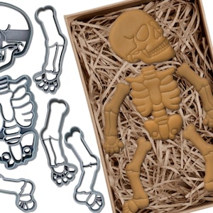 May include: A set of cookie cutters in the shape of a skeleton. The cutters are made of metal and are silver in colour. The set includes a skull, rib cage, and two sets of arms and legs.