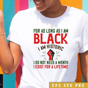 以下が含まれることがあります： 「FOR AS LONG AS I AM BLACK I AM HISTORIC I DO NOT NEED A MONTH I EXIST FOR A LIFETIME」という文字が書かれた白いTシャツ。文字は赤と緑で書かれており、中央には緑と赤のデザインが施された黒い拳が描かれている。